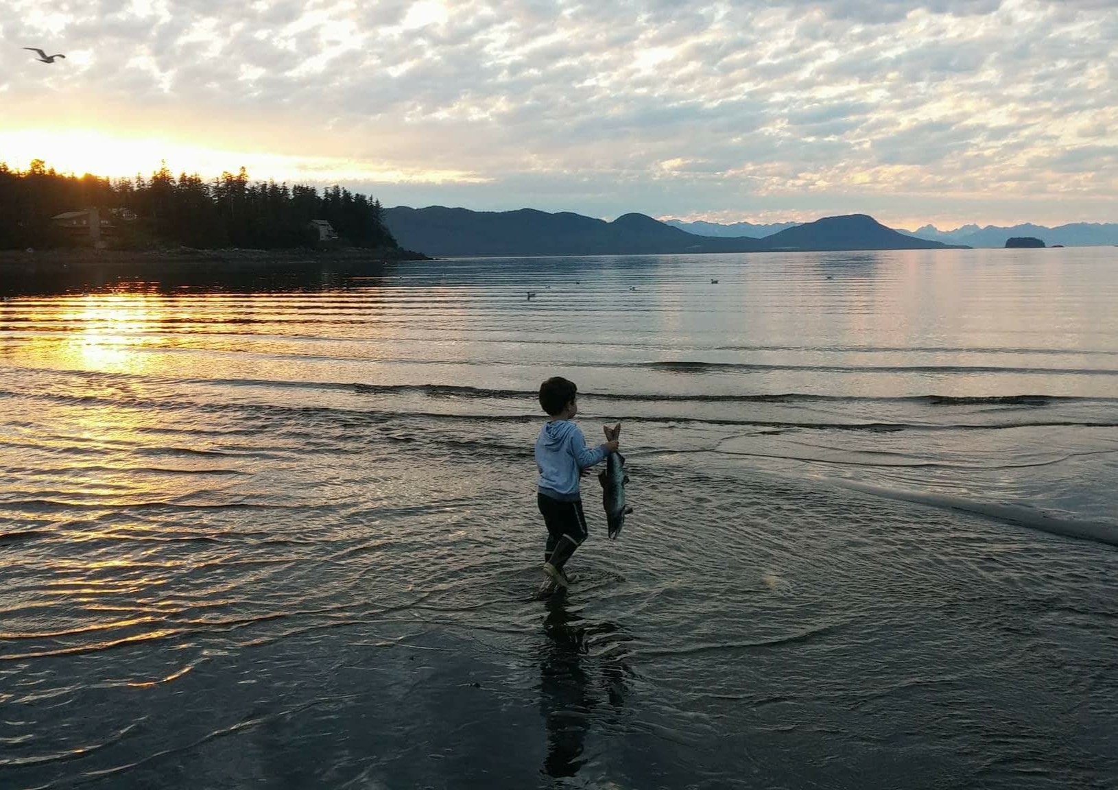 A child holds a salmon in front of a coastal inlet in Southeast Alaska. 