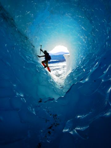 An ice climber climbs an ice tube on a glacier.