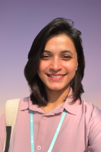 A young woman stands in front of a purple background.