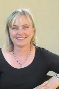 Portrait of a woman with blonde hair. She is smiling and wearing a black top