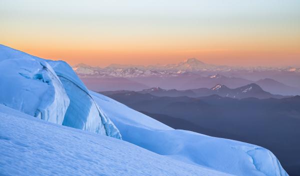 A snowy mountainside in front of mountain ranges